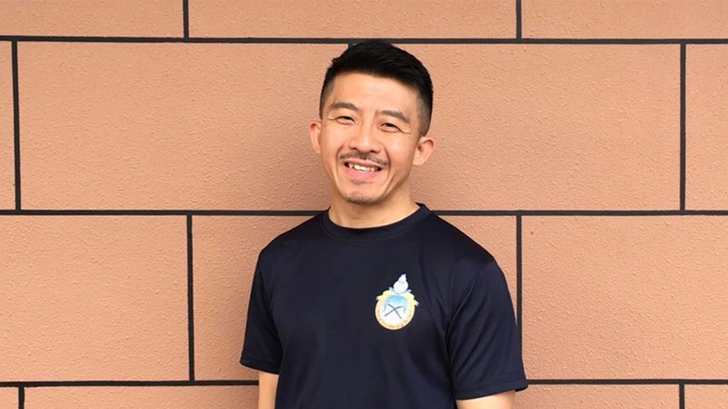 man in blue shirt posing in front of brick wall