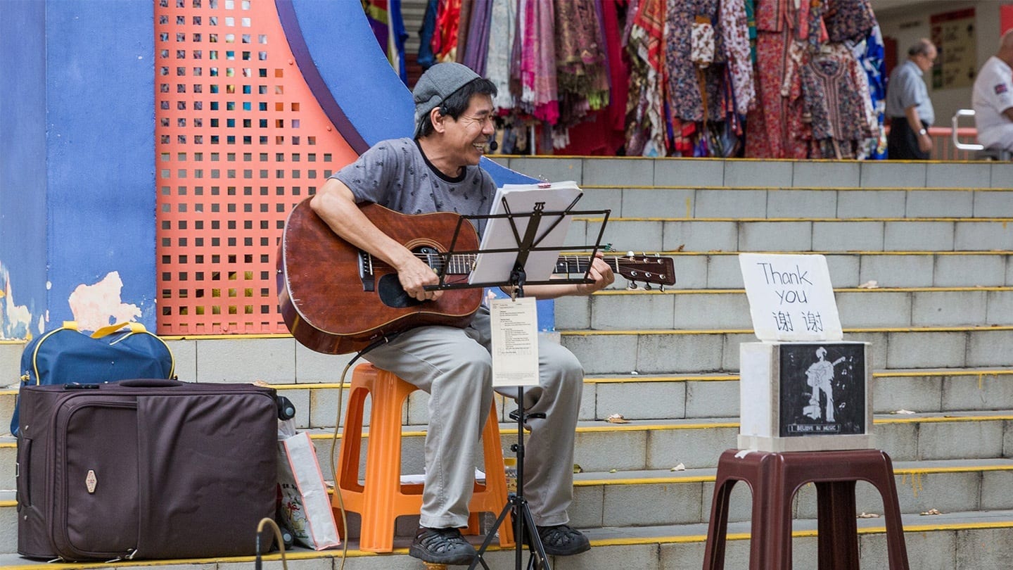 old man busking with a guitar next to a sign that says thank you