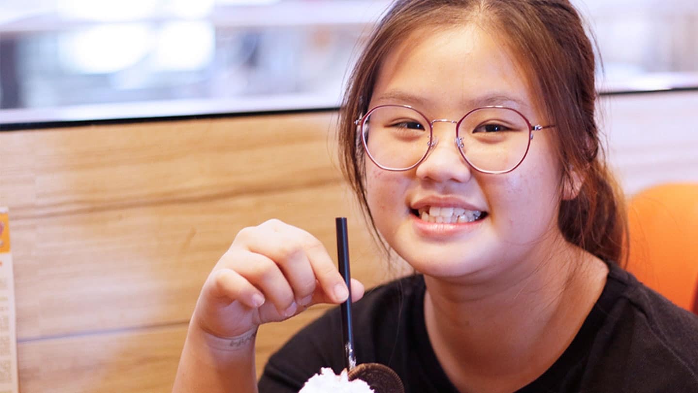 girl in round glasses and ponytail with a glass of drink topped with whipped cream and an oreo