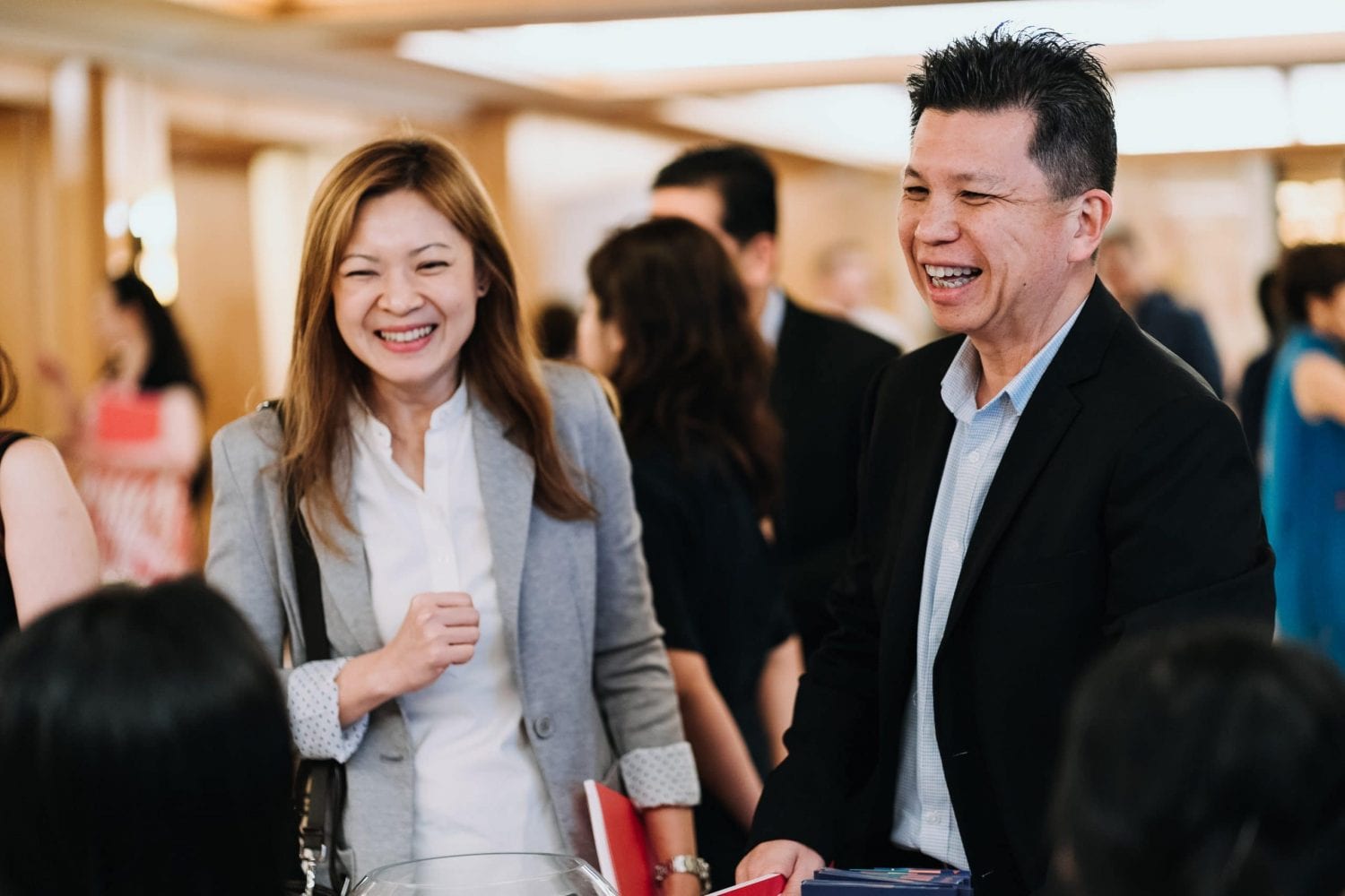 woman in grey blazer and man in black suit jacket holding red booklets