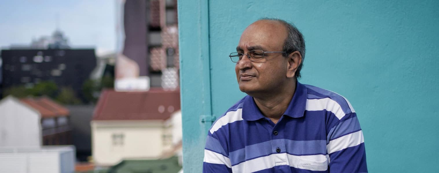 indian man wearing a dark blue shirt posing in front of a light blue wall