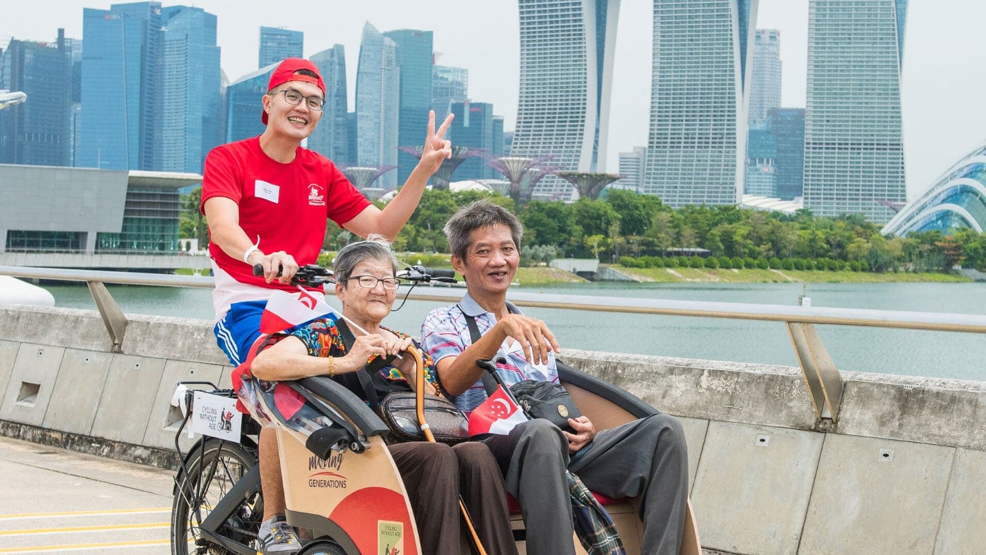 volunteer in red shirt and cap ferrying an elderly couple around on a trishaw