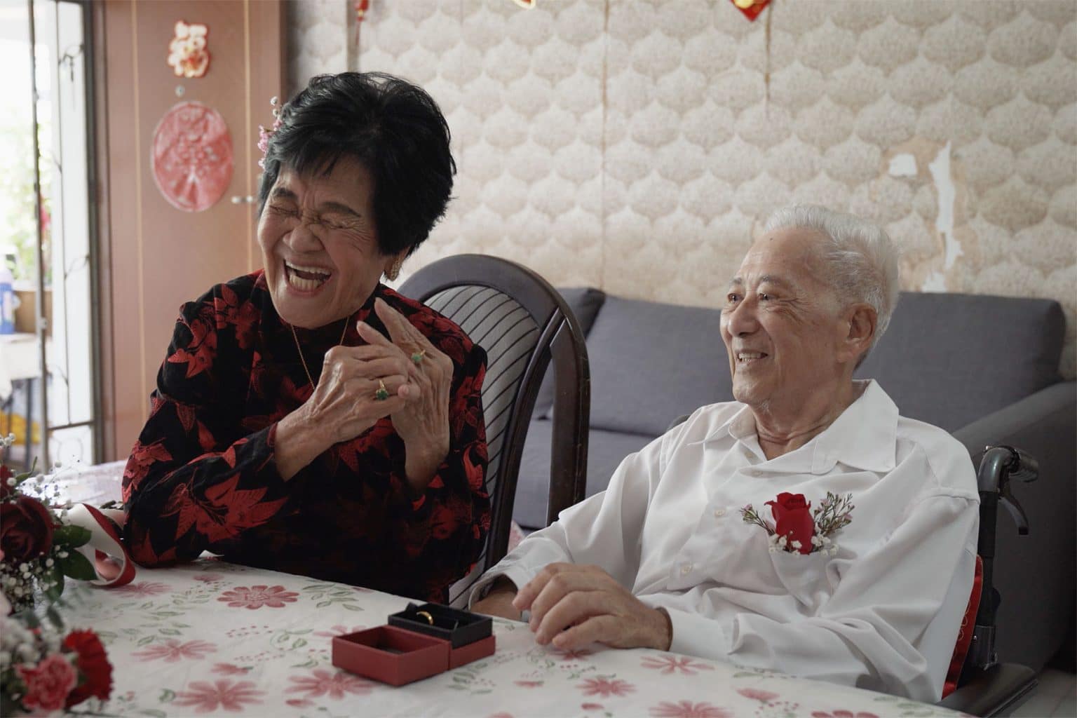 elderly woman in red and black blouse with her husband in white