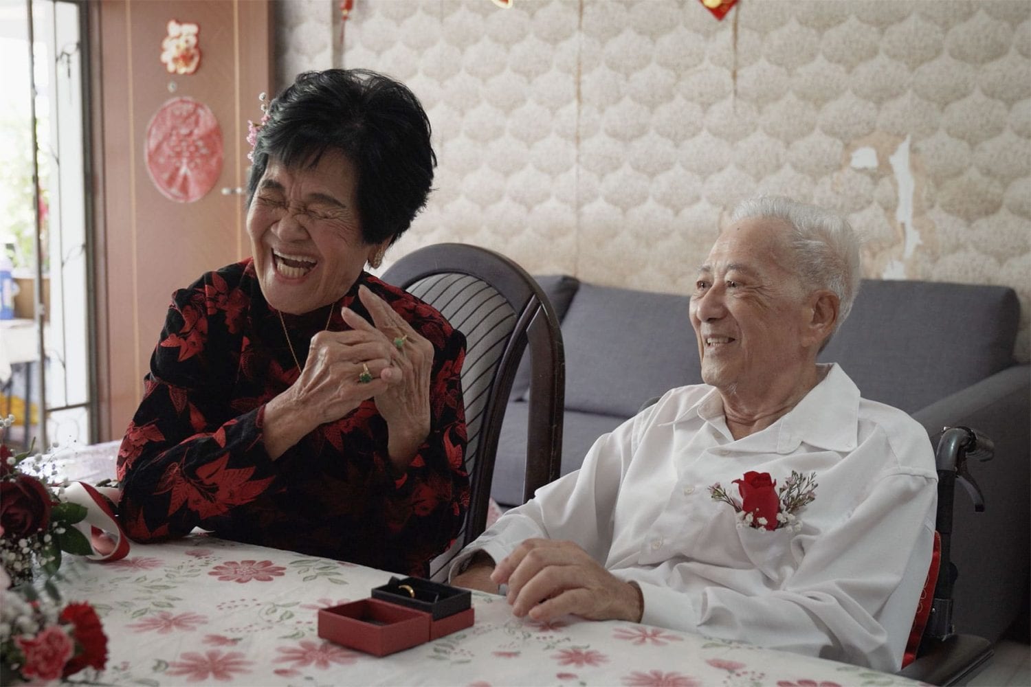 elderly woman in red and black blouse with her husband in white