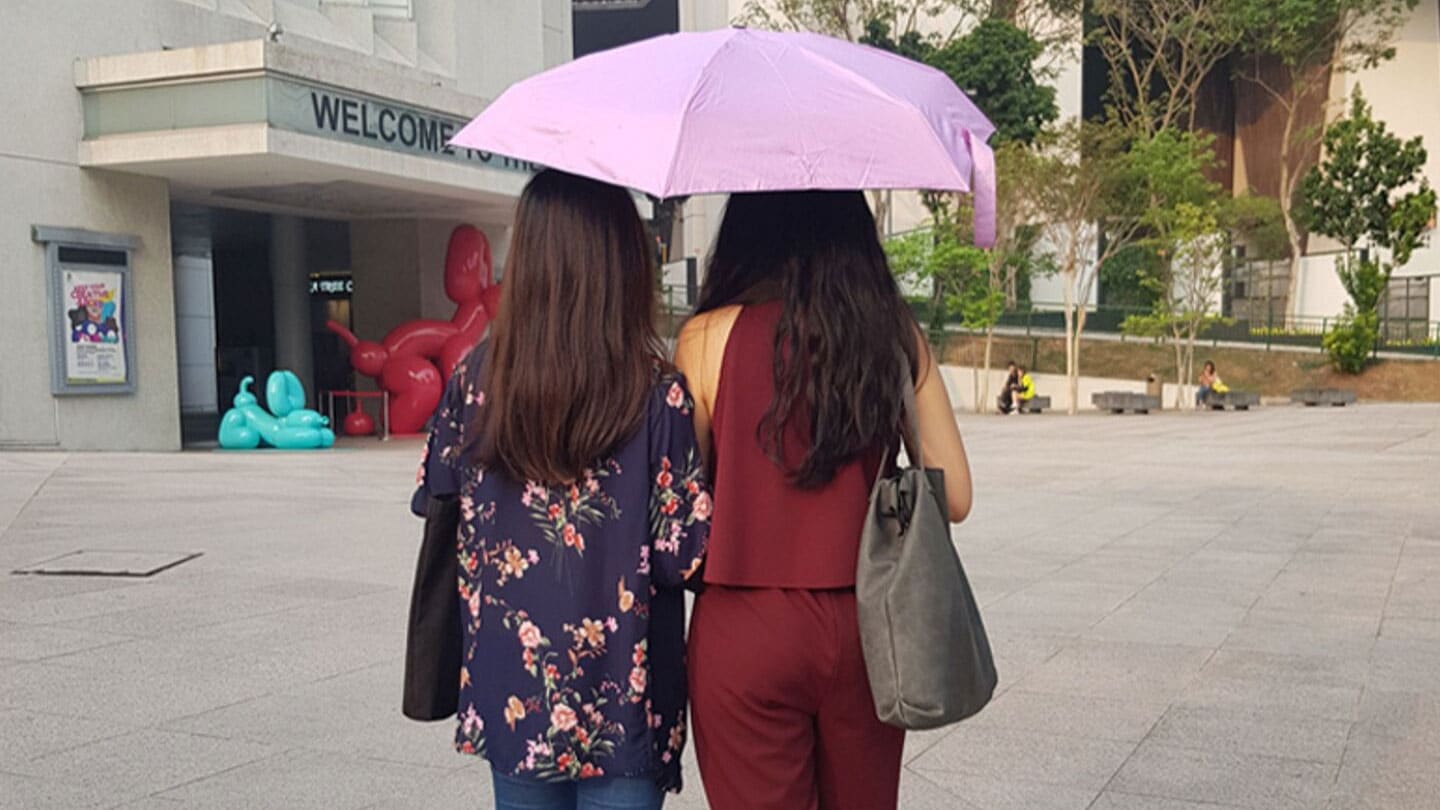 girls in red and blue sharing a light purple umbrella