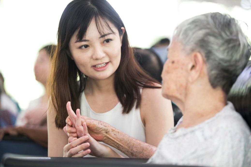 woman in white blouse holding hand of elderly woman with grey hair