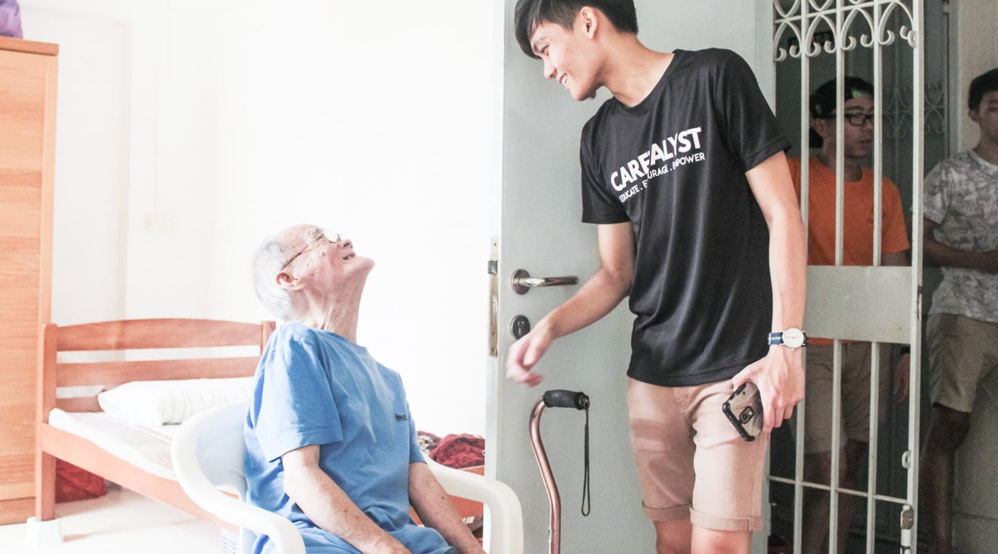 male youth in black shirt and elderly man in blue shirt smiling at each other