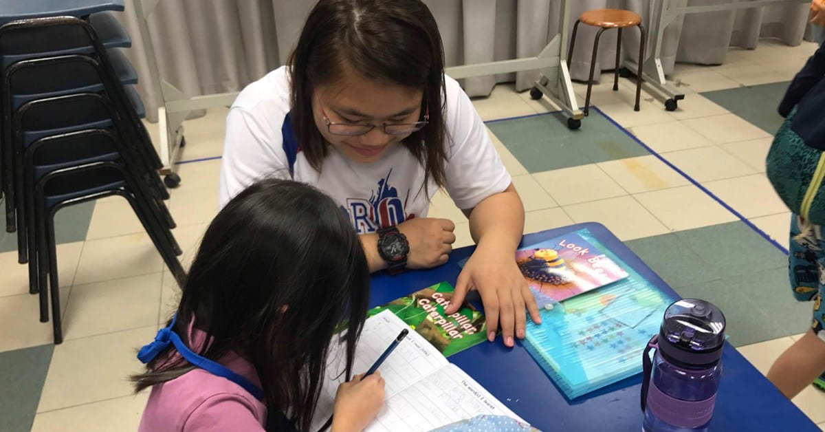 woman in white shirt helping a girl in a pink shirt do her homework