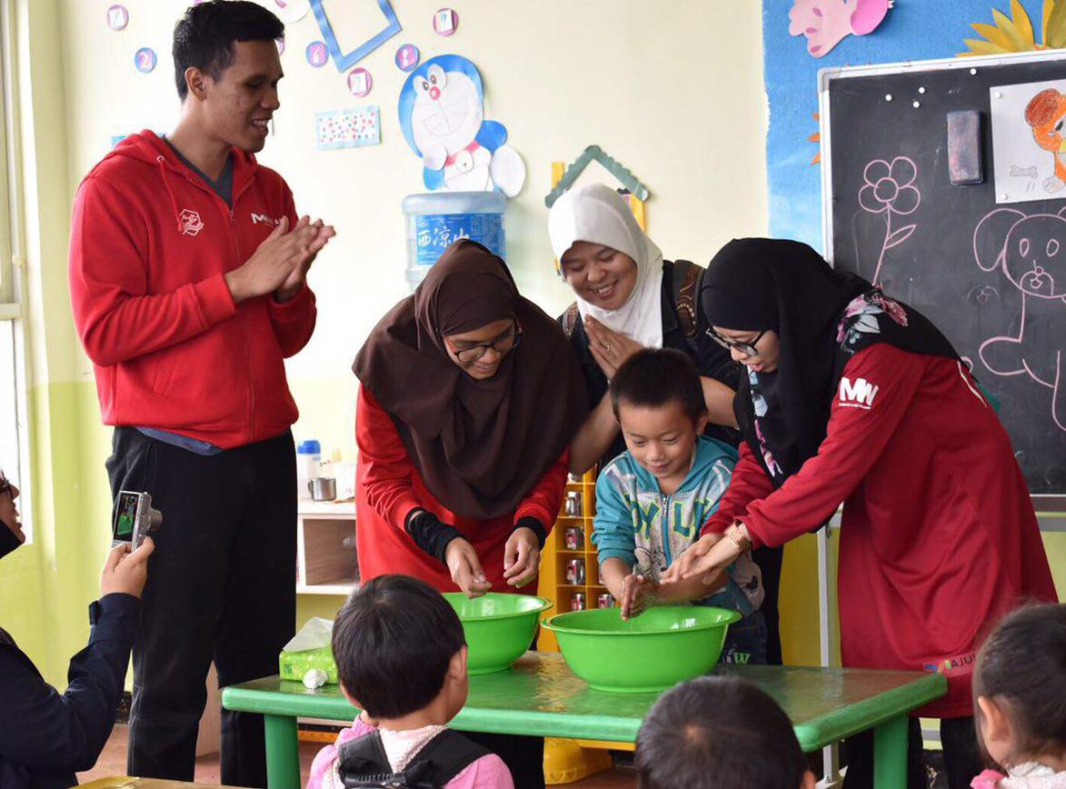 three malay women in tudungs and malay man clapping as a boy washes his hands in a basin