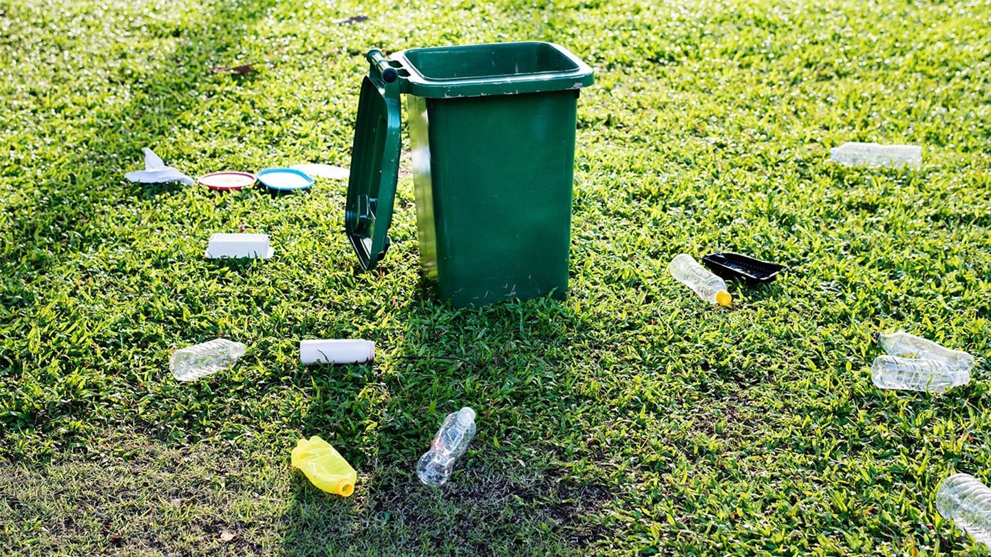 green garbage bin with plastic bottles littered around it on the grass