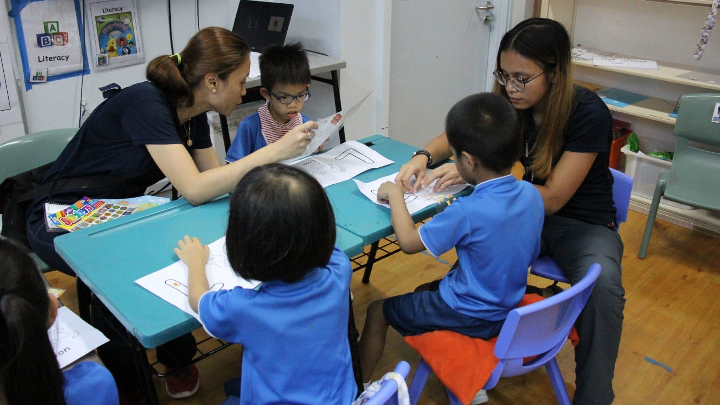 two female teachers teaching three kindergarteners in blue shirts