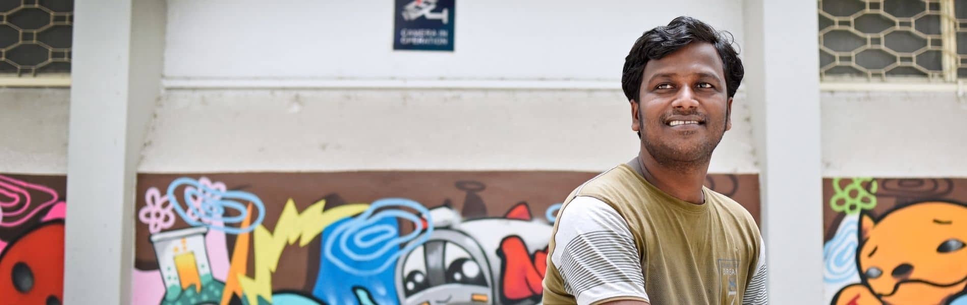 indian man smiling in front of graffiti wall