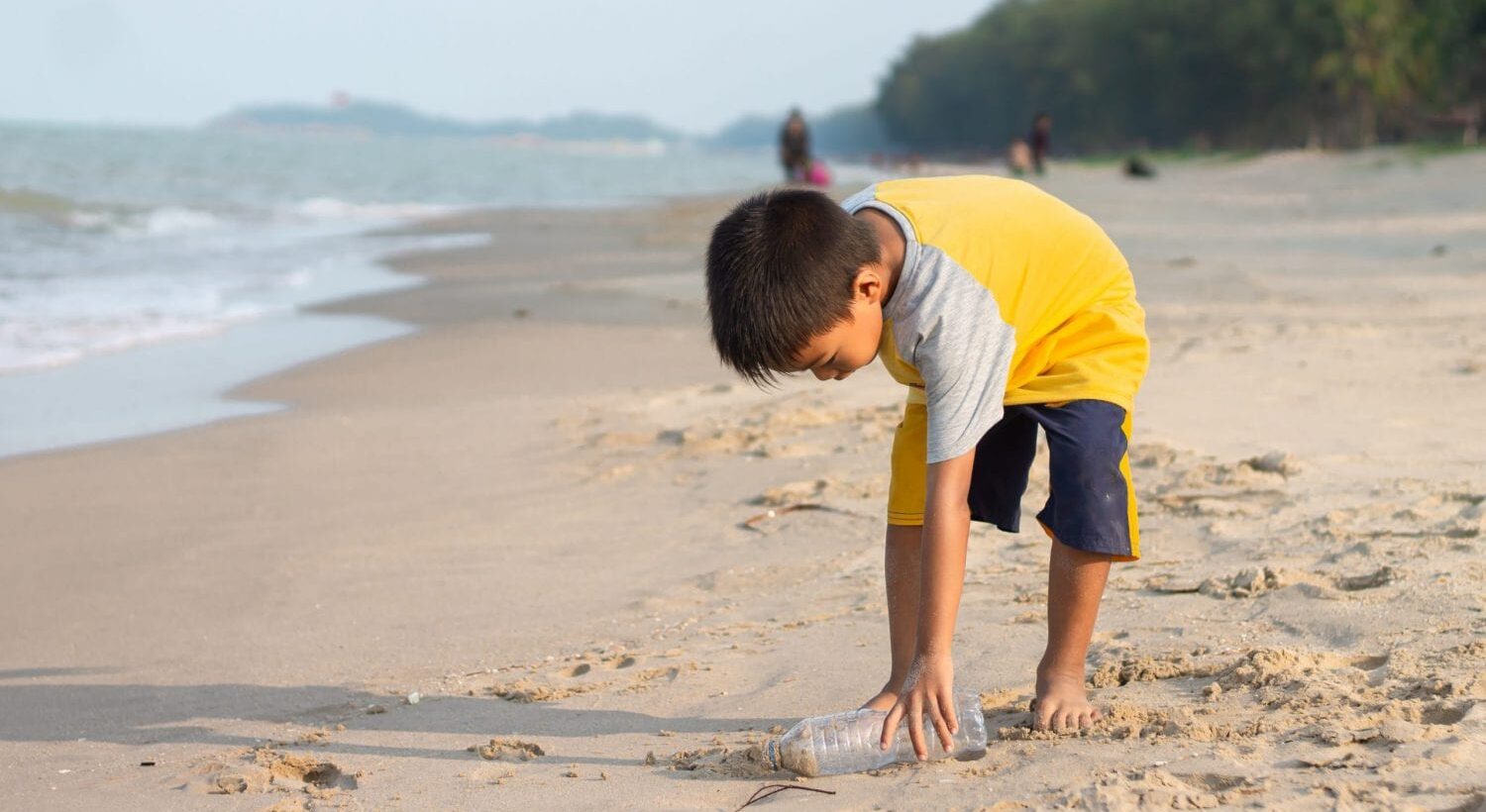 boy in yellow shirt picking up bottle on the beach