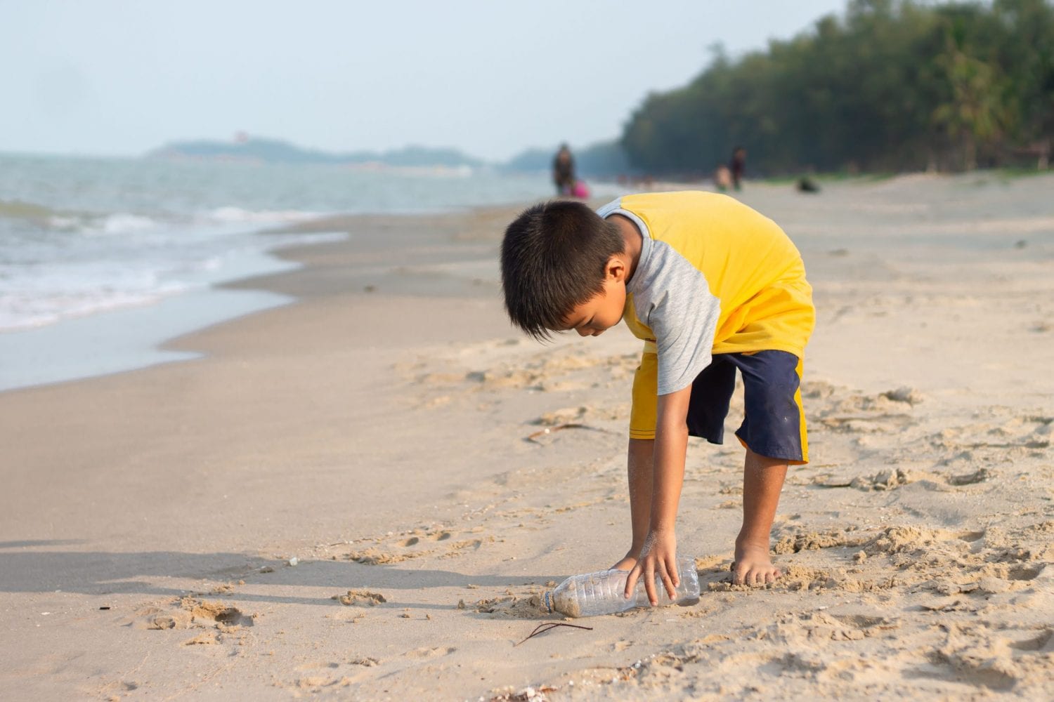 boy in yellow shirt picking up bottle on the beach