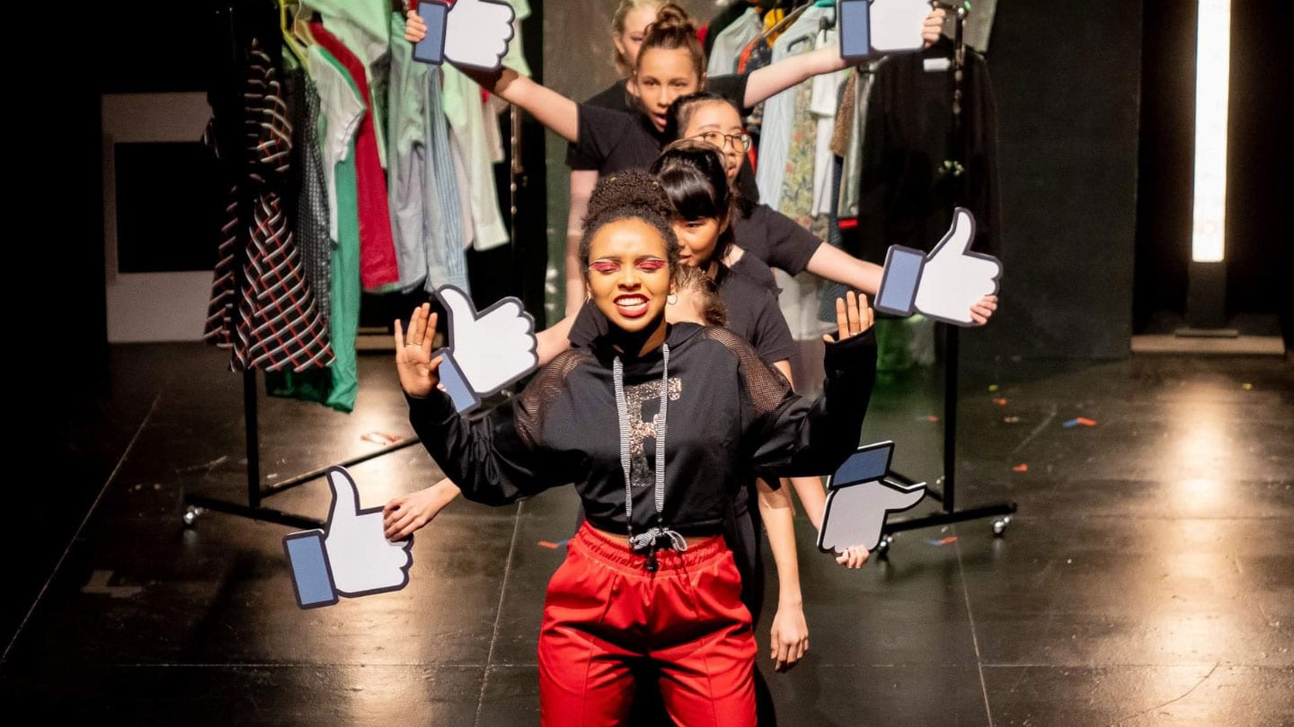 women holding facebook thumbs up signs performing on stage with racks of clothes in background