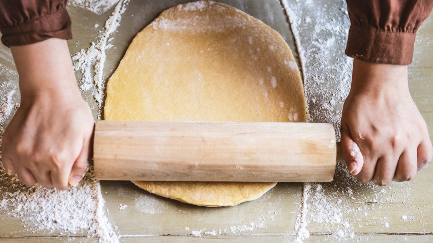 someone flattening dough into a circle using a rolling pin