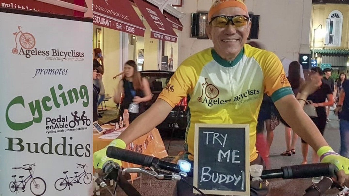 ageless bicyclists participant riding a bike with a sign that says try me buddy