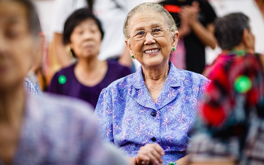 old lady in blue blouse with green stud earrings smiling straight into the camera