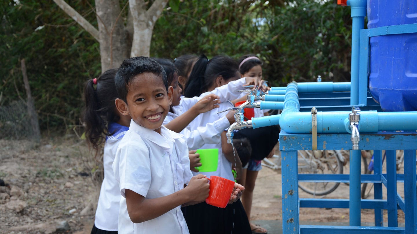 schoolchildren collecting water from a row of pipes