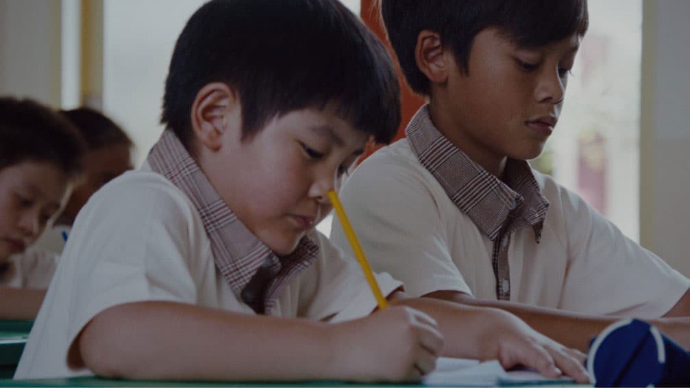 chinese and malay boy in brown uniforms taking notes in their notebook during a lesson