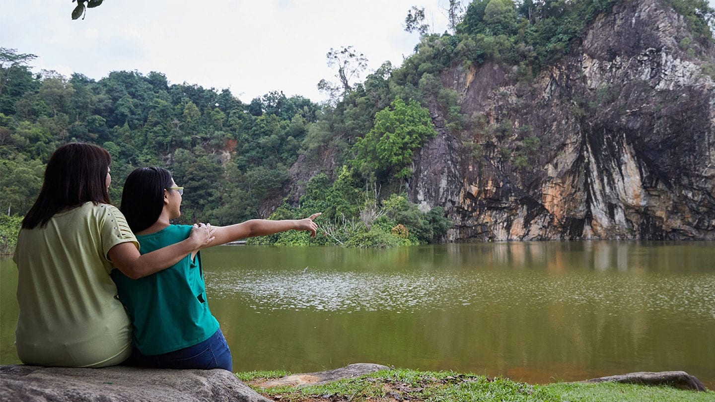 two women in green shirts sitting in front of a body of water and an arrangement of karsts