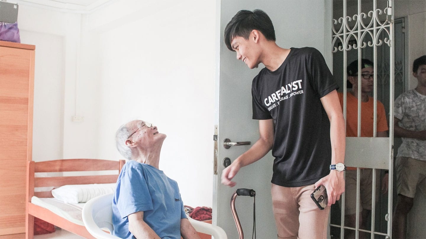 male youth in black shirt and elderly man in blue shirt smiling at each other