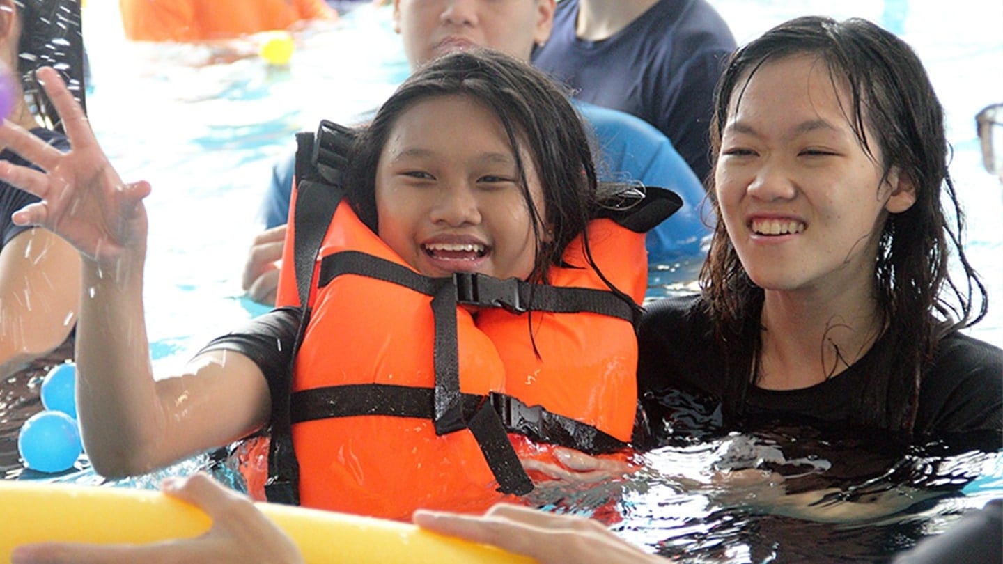 girl in orange life jacket with woman in long hair and black shirt behind her