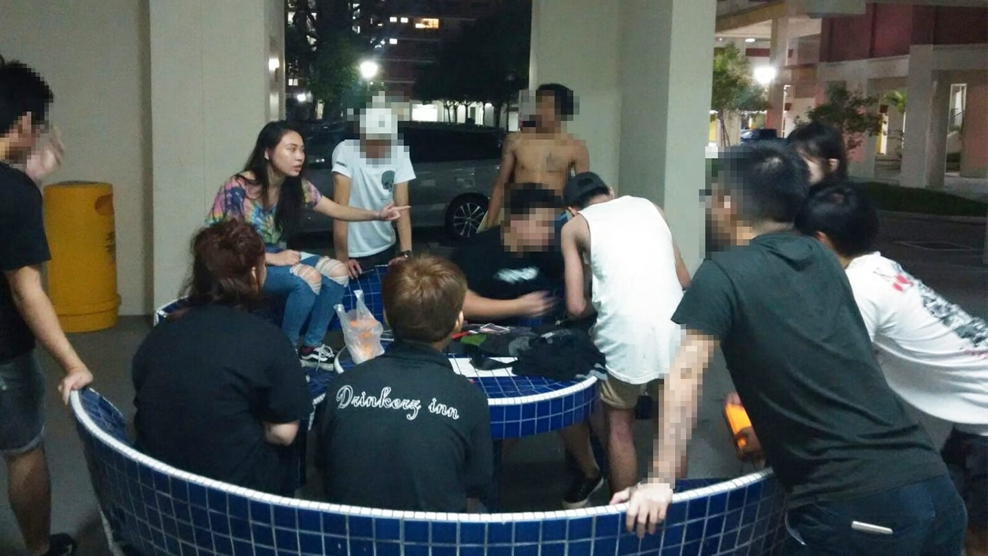 people gathered around a void deck table with the faces of four men censored out