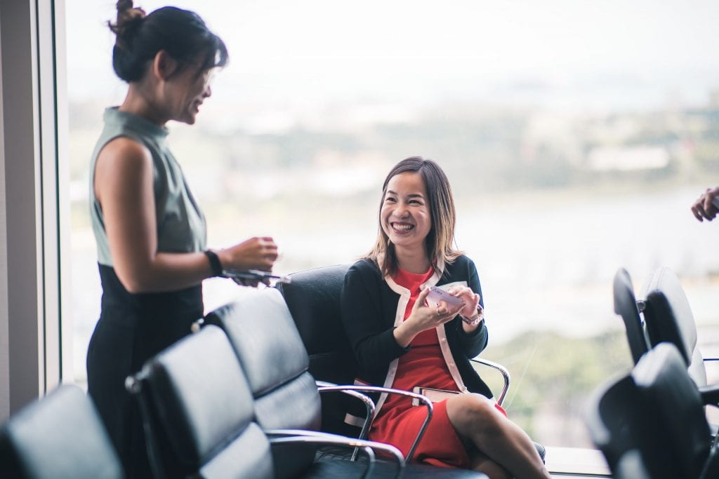 woman in orange dress and blazer smiling up at woman in french twist