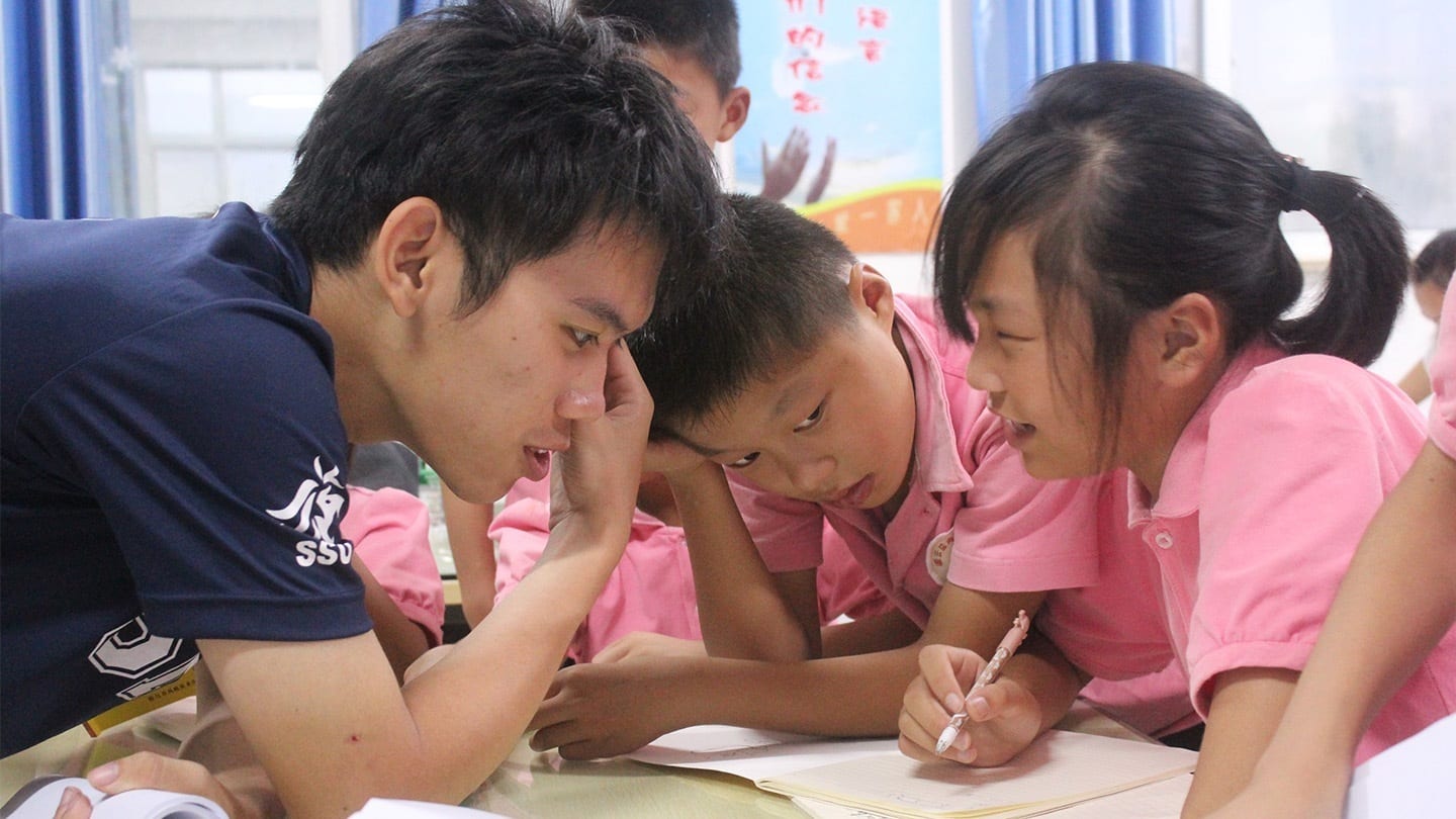 man in blue shirt talking to young children in pink shirts