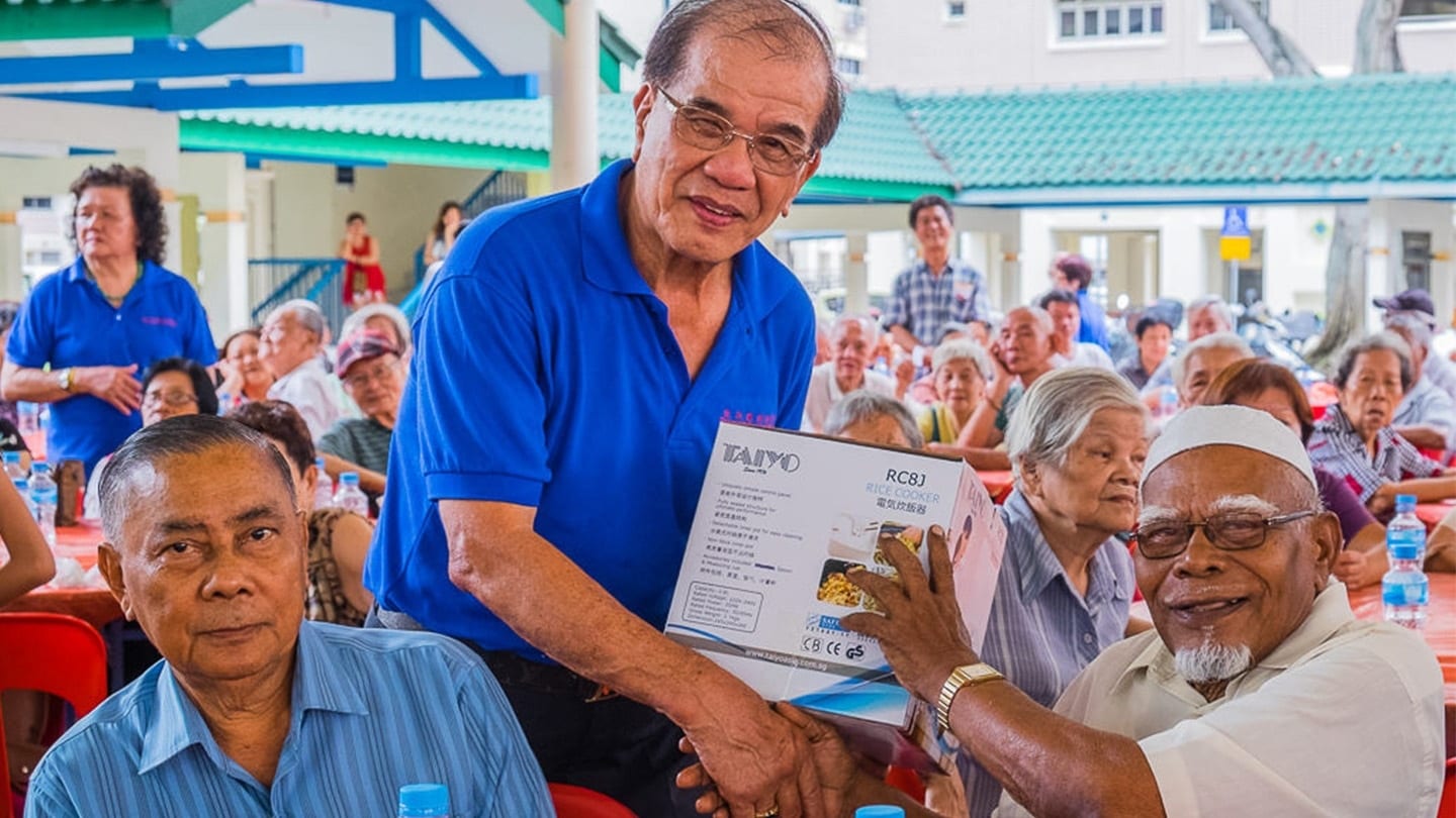 volunteer in blue giving rice cooker to elderly beneficiary