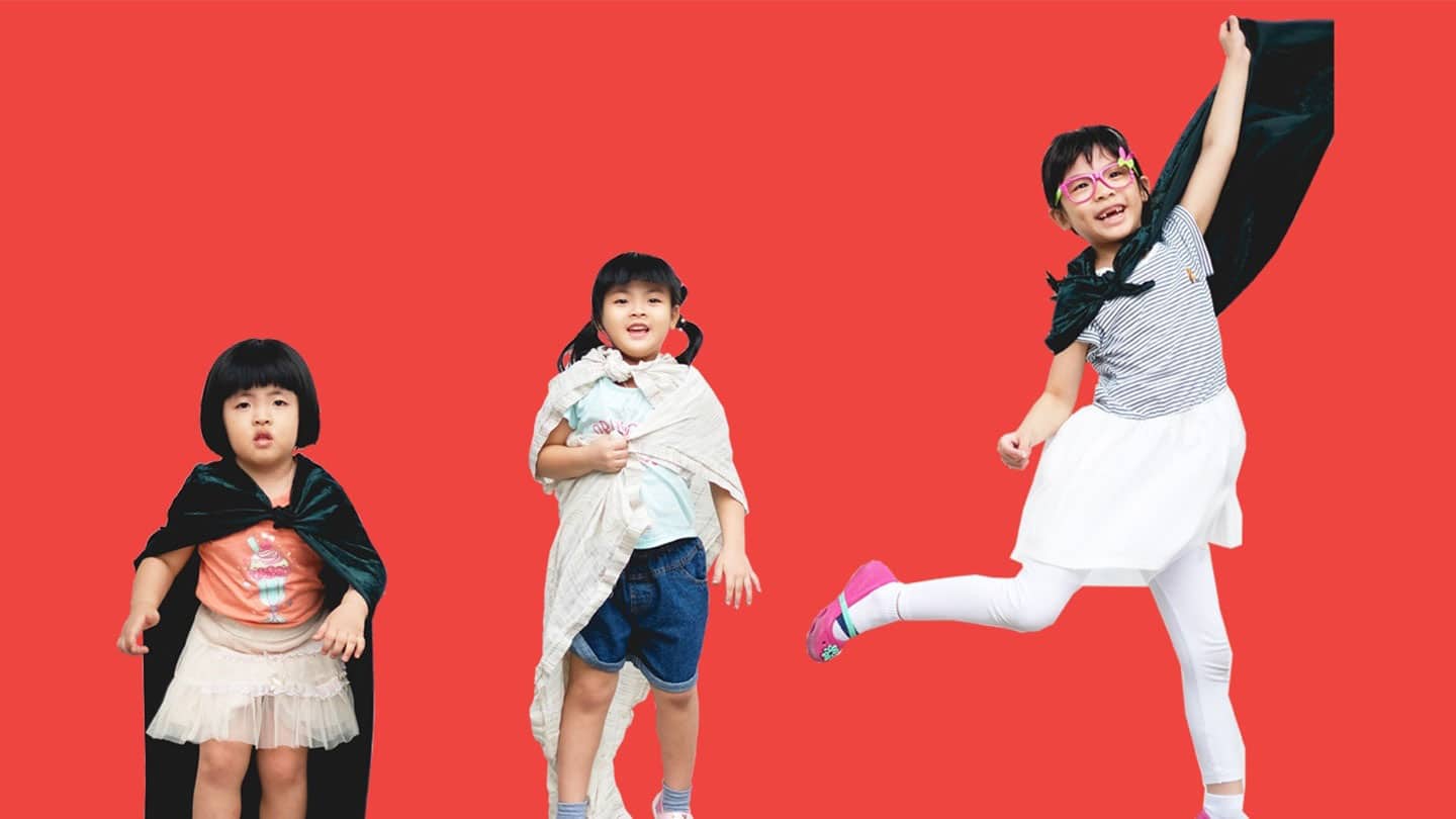 three girls in superhero capes against red background