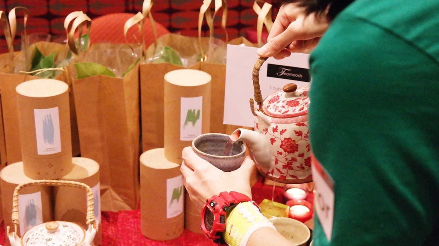 woman pouring tea from a red porcelain kettle into a teacup