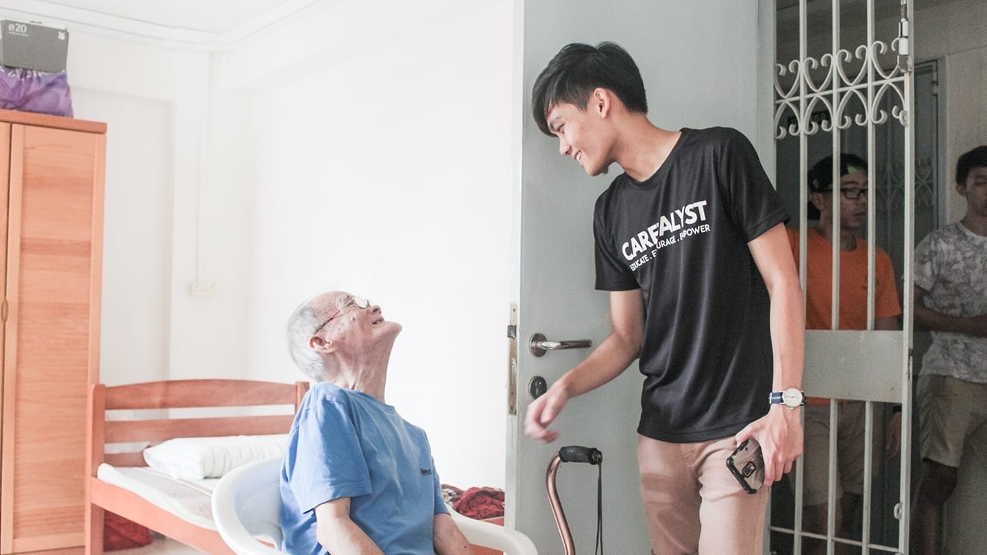 male youth in black shirt and elderly man in blue shirt smiling at each other