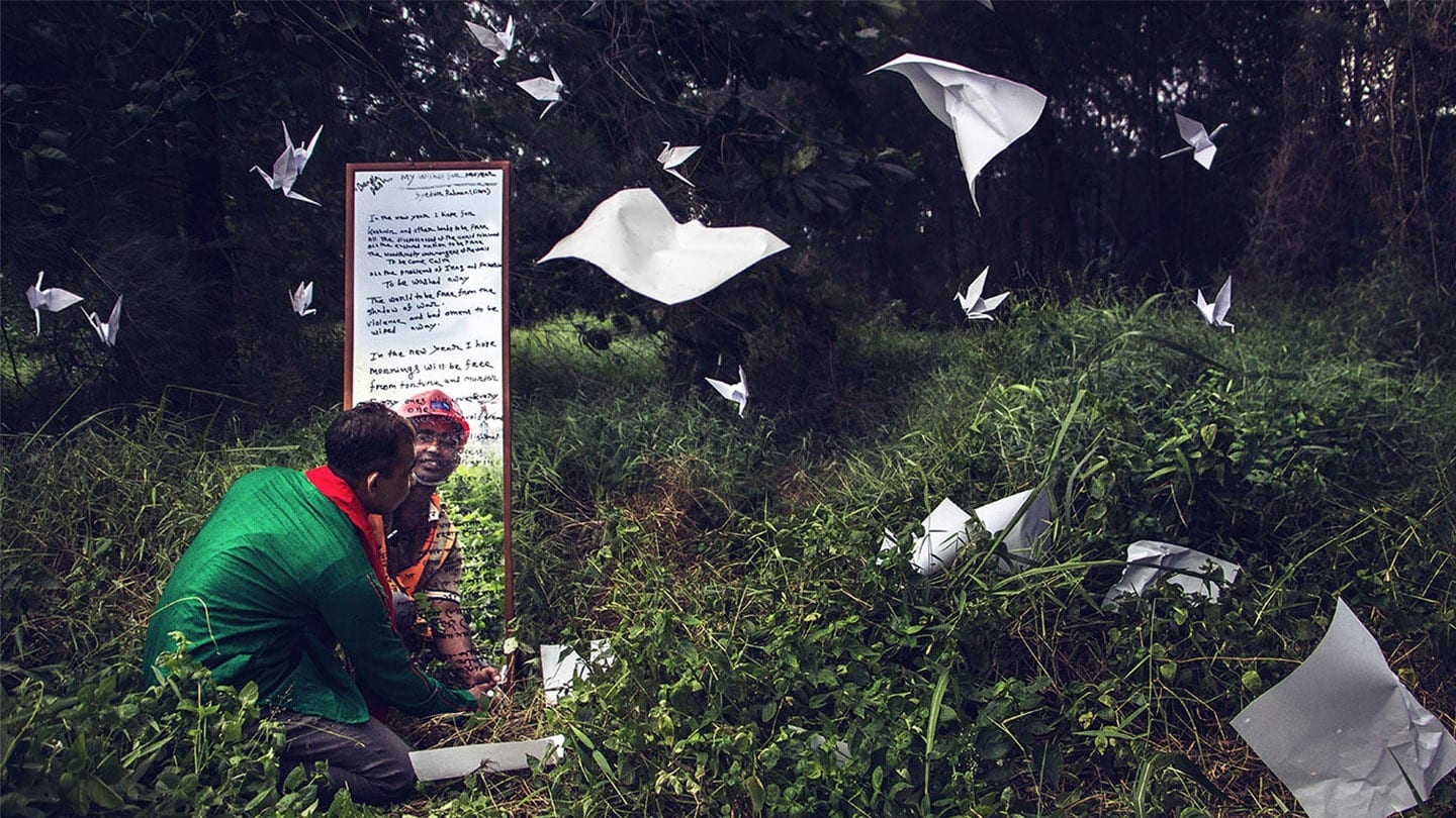 indian man looking into mirror at his own reflection as papers fly about