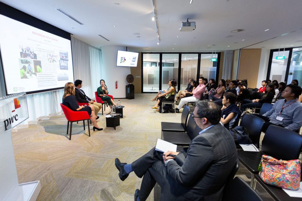 three speakers in red chairs giving a talk to a room of people in suits at pwc