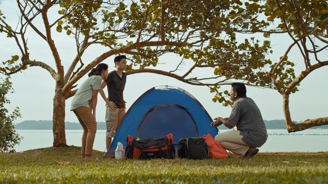 two men and one woman standing around a tent by the beach