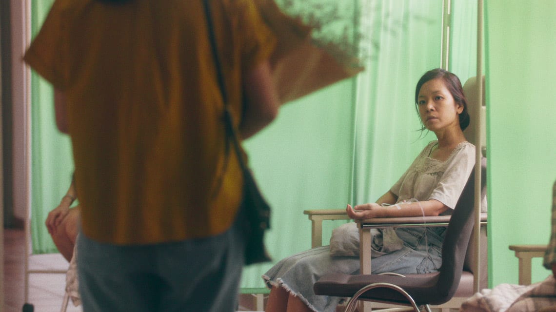 woman with tube in her arm sitting in a hospital chair and looking up at faceless person in the foreground