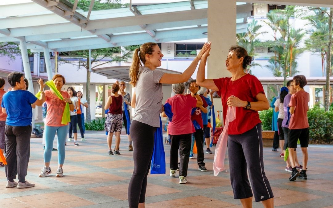 caucasian lady high-fiving an elderly woman in a red shirt