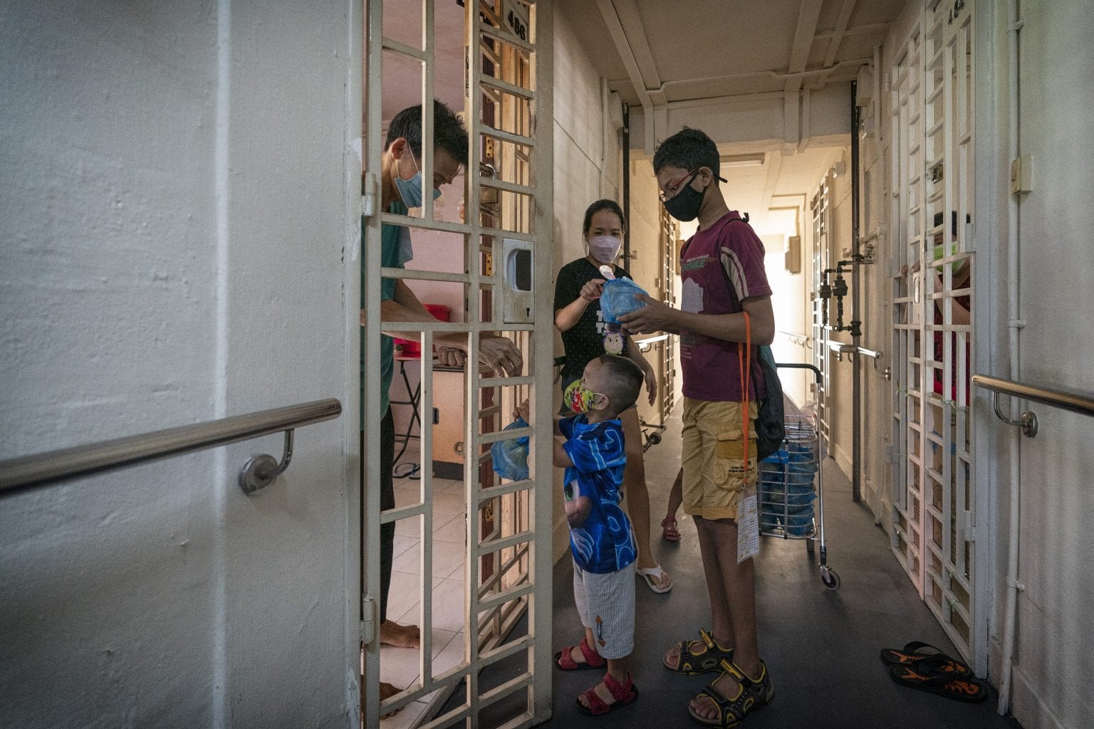 boys in red and blue shirts passing food through the door to elderly tenant