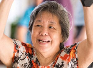 elderly woman in orange and black floral shirt with arms raised above her head