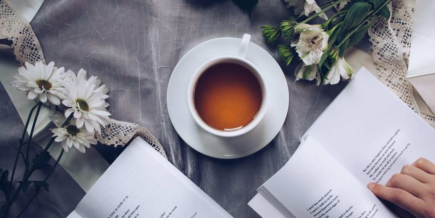 a cup of drink, surrounded with open books and flowers